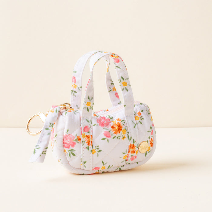 The Endless Daydream Cream Itty Bitty Duffle Bag Charm by the-darling-effect is a small quilted handbag with a pink, orange, and green floral pattern on white, featuring two handles, a gold zipper, keyring, and chic duffle bag charm accessory.