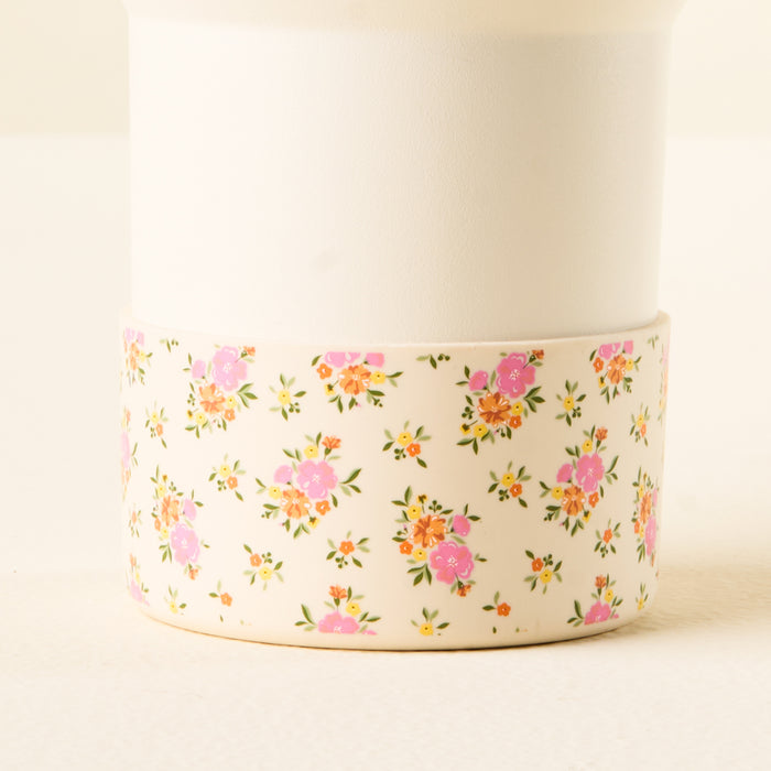 The-darling-effect Endless Daydream Cream Tumbler features a white top, a floral lower section with pink, orange, and yellow flowers on cream, and a silicone boot for protection against tumbler dents.