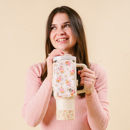 A smiling woman with long brown hair, in a pink ribbed sweater, holds the-darling-effect’s Endless Daydream Cream Tumbler with a protective silicone boot, standing against a light beige background.