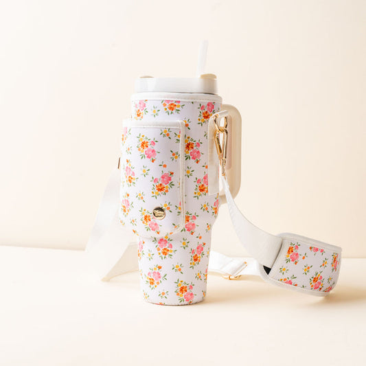 The Endless Daydream Cream Tumbler Sling by the-darling-effect features a colorful floral pattern, adjustable strap, gold hardware, small pocket, and holds a tumbler with lid and straw—perfect for hands-free carrying.