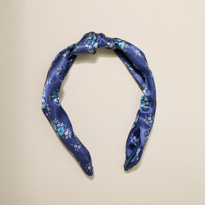 The Darling Effect’s Endless Daydream Navy Classic Twist Headband features small light blue and white flowers with green leaves on a navy background—a versatile accessory perfect for any occasion.