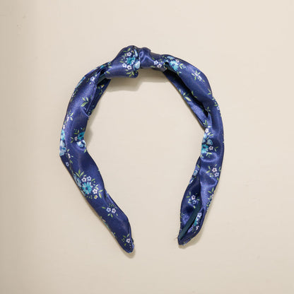 The Darling Effect’s Endless Daydream Navy Classic Twist Headband features small light blue and white flowers with green leaves on a navy background—a versatile accessory perfect for any occasion.