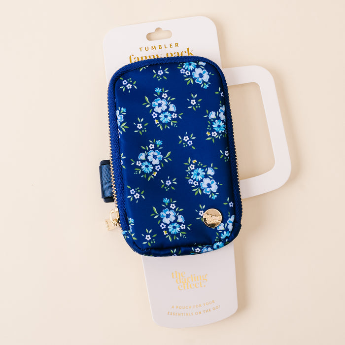 The-darling-effect's Endless Daydream Navy Tumbler Fanny Pack has a chic floral print, zipper, and gold charm. Water resistant, it's displayed on a white card reading "The Darling Effect" and "A Pouch for Your Essentials on the Go!.