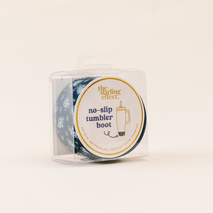 The Endless Daydream Navy Tumbler Silicone Boot by the-darling-effect features a blue floral design and is displayed in a clear plastic box. A round label shows "the-darling-effect," an illustration, and describes it as a no-slip tumbler boot.