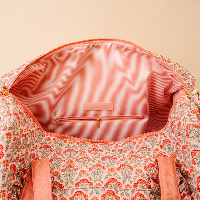 The Darling Effect Everbloom Dusty Rose On-the-Go Quilted Weekender Bag features a light pink floral print, striped pink and white lining, an interior zip pocket, branded tag, and an adjustable shoulder strap for easy travel.
