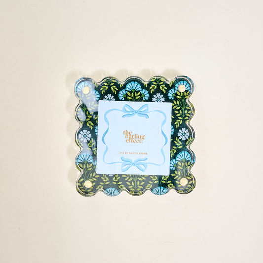 The Everbloom Forest Green Little Moments Acrylic Picture Frame by The Darling Effect features a scalloped edge with a dark green floral design, holding a light blue card and ribbon border. Fits 2.5x2.5 photos.