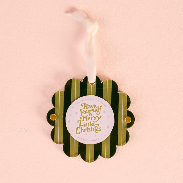 The Darling Effect's Evergreen Stripes Scalloped Round Picture Frame Ornament features green stripes, a scalloped design, gold and pink "Have Yourself a Merry Little Christmas" text, and a white ribbon, shown on a light pink background.