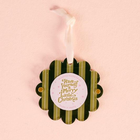 The Darling Effect's Evergreen Stripes Scalloped Round Picture Frame Ornament features green stripes, a scalloped design, gold and pink "Have Yourself a Merry Little Christmas" text, and a white ribbon, shown on a light pink background.