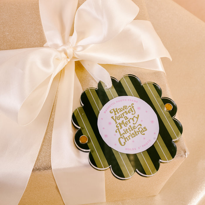 A gold gift box with a white satin ribbon and green & gold "Have Yourself a Merry Little Christmas" tag—perfect for gifting The Darling Effect’s Evergreen Stripes Scalloped Round Picture Frame Ornament.