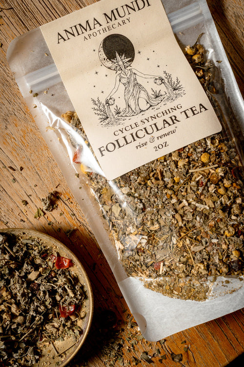A clear stand-up pouch of Anima Mundi Apothecary Cycle Syning Follicular Tea with a beige label, shown on a rustic wooden surface with a small bowl of loose tea nearby.