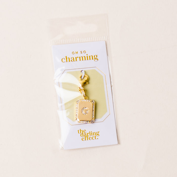 The-darling-effect's G Jewelry Charm Initial Letter Gold features a rectangular gold-plated brass charm with a central clear gem on a keyring, packaged on an "Oh so charming" card and photographed against a light background.