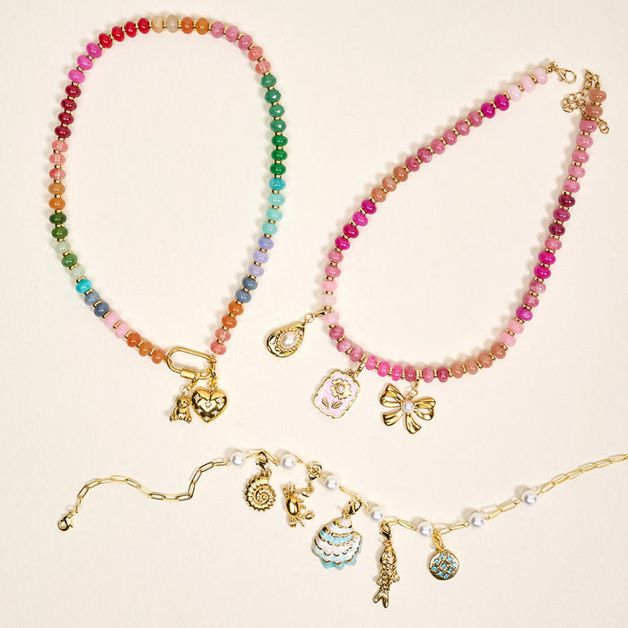 Three colorful the-darling-effect necklaces are shown on a light background, each adorned with gold-plated brass charms like hearts, butterflies, bows, and G Jewelry Charm Initial Letter Gold. One necklace has a gold chain with dangling charms.