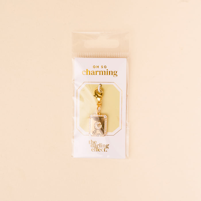 The-darling-effect’s G Jewelry Charm Initial Letter Gold features a gold-plated brass charm with rhinestones and a rectangular frame, hanging from a lobster clasp on an “Oh So Charming” card—perfect for lovers of personalized jewelry.