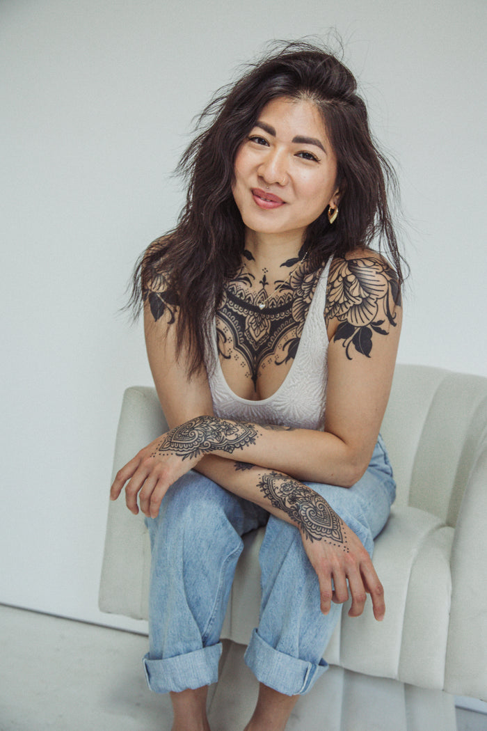 Woman with tattoos sitting on a white couch against a plain background