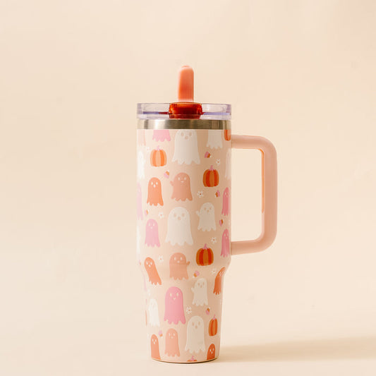 The Darling Effect Ghost Party 40 oz Lifestyle Flip Straw Tumbler, in pale pink with ghost and pumpkin designs, features triple-walled insulation, a clear lid, a matching pink straw, and a handle. Displayed against a light beige background.