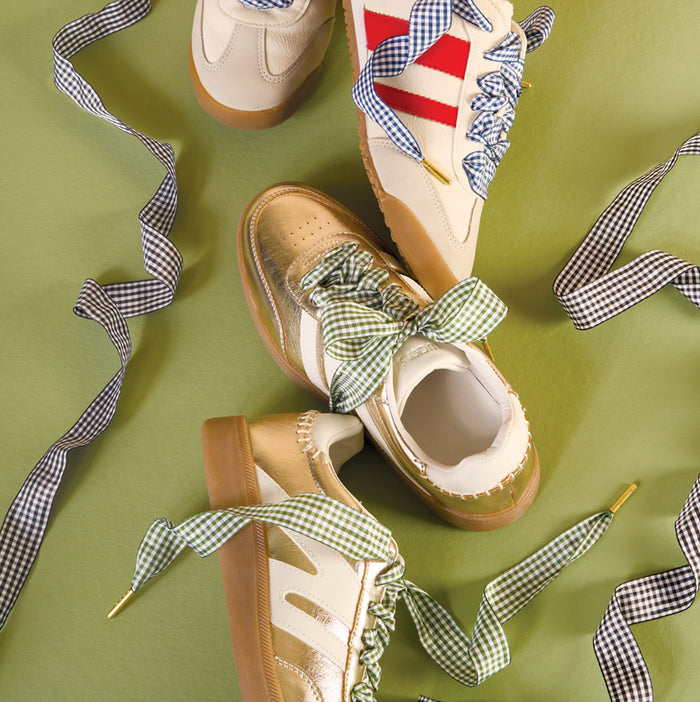 Three pairs of retro sneakers with gum soles and striped sides, each featuring The Darling Effect's Gingham Black Step It Up Shoelaces, are displayed on a green background.