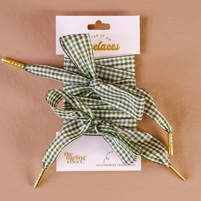 Gingham Green Step It Up Shoelaces by The Darling Effect feature green and white gingham with gold tips, tied in bows and displayed on a branded card. Durable laces to stylishly accessorize your shoes.