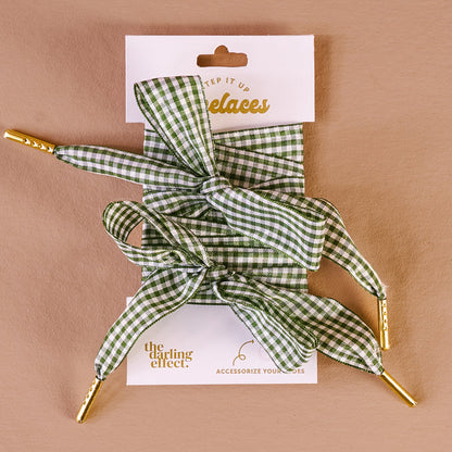 Gingham Green Step It Up Shoelaces by The Darling Effect feature green and white gingham with gold tips, tied in bows and displayed on a branded card. Durable laces to stylishly accessorize your shoes.