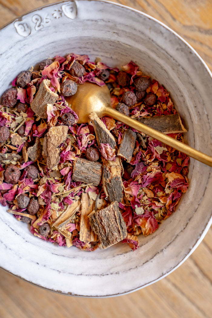 Herbal tea mix with a gold spoon in a white bowl on a wooden surface