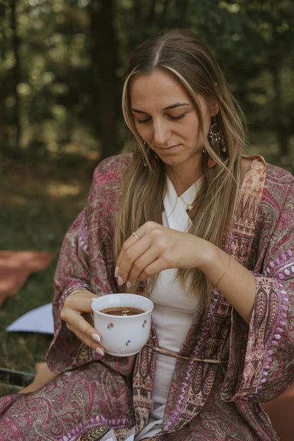 Woman in a patterned robe holding a cup outdoors