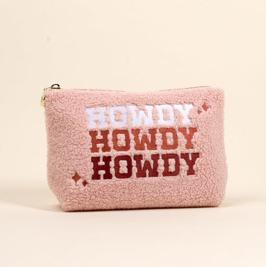 The Howdy Howdy Howdy Teddy Pouch by the-darling-effect is a small, soft pink sherpa zip pouch featuring "HOWDY" three times in white, light brown, and dark brown bold letters with star accents.