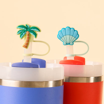 The Island Escape Straw Topper Set by the-darling-effect includes two leak-resistant, colorful tumblers—one blue with a palm tree topper and one red with a blue seashell topper—perfect for fun drinkware against a light beige background.