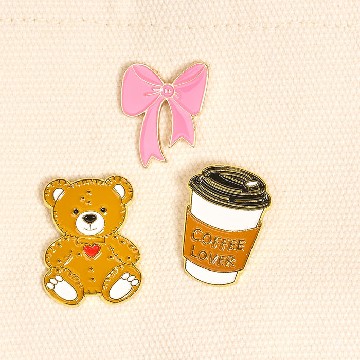 Latte Love The Pin Pack by The Darling Effect features three pins on light fabric: a pink bow, a teddy bear with heart, and a coffee cup labeled COFFEE LOVER—an expressive collectible set for any pin collection.