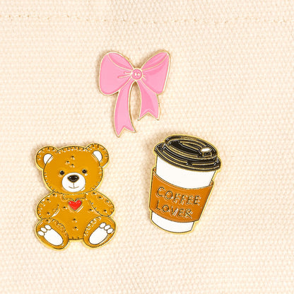 Latte Love The Pin Pack by The Darling Effect features three pins on light fabric: a pink bow, a teddy bear with heart, and a coffee cup labeled COFFEE LOVER—an expressive collectible set for any pin collection.