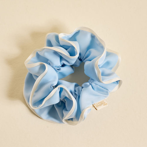 The Darling Effect Light Blue Ruffle Up Scrunchie features a voluminous, oversized design with white trim edges, gentle hold, and a small branded label—shown on a cream background.
