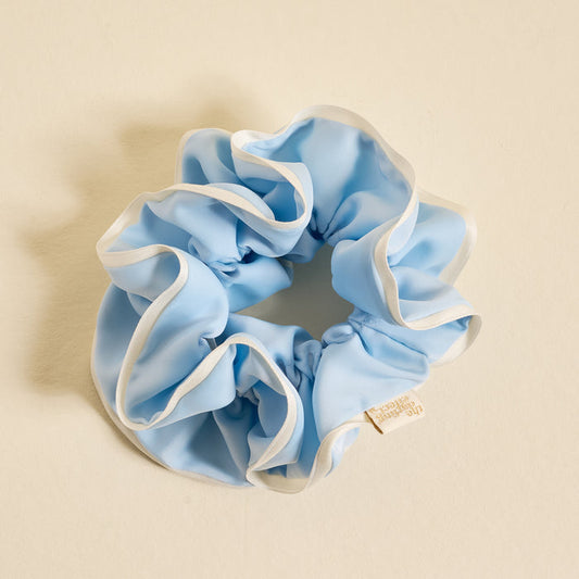 The Darling Effect Light Blue Ruffle Up Scrunchie features a voluminous, oversized design with white trim edges, gentle hold, and a small branded label—shown on a cream background.