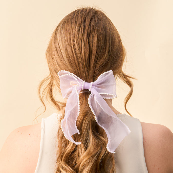 Back view of a woman with long, wavy auburn hair styled with the-darling-effect's Lilac Sheer Pearl Hair Bow, adorned with small white pearls.