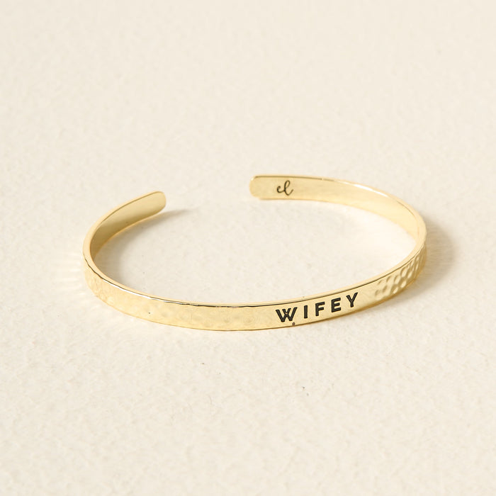 The Darling Effect's Little Reminder Cuff is a 14k gold plated, hammered bracelet engraved with WIFEY and a small script "cl" inside—beautifully displayed and gift-ready for celebrating someone special.