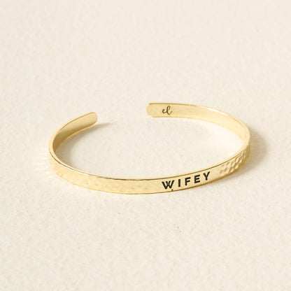 The Darling Effect's Little Reminder Cuff is a 14k gold plated, hammered bracelet engraved with WIFEY and a small script "cl" inside—beautifully displayed and gift-ready for celebrating someone special.