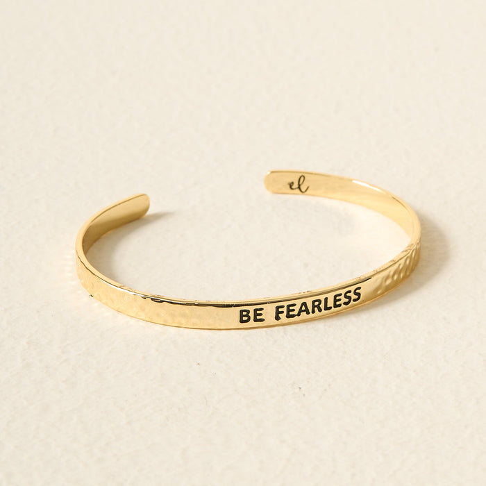 The Darling Effect’s Little Reminder Cuff: 14k gold-plated, hammered finish, engraved with BE FEARLESS in bold black letters. An open-ended bracelet on a neutral background—gift-ready inspiration for every day.
