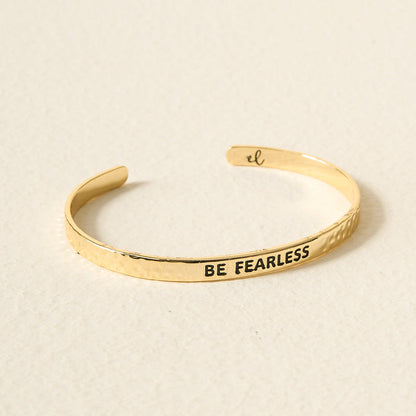 The Darling Effect’s Little Reminder Cuff: 14k gold-plated, hammered finish, engraved with BE FEARLESS in bold black letters. An open-ended bracelet on a neutral background—gift-ready inspiration for every day.
