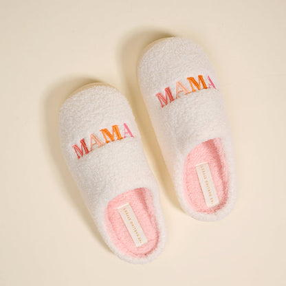 The Darling Effect's Mama Fuzzy Slippers feature soft white exteriors, pink interiors, and colorful "MAMA" embroidery on top—perfectly cozy and stylish for home comfort.