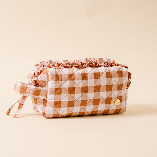Quilted cosmetic pouch with a brown and white checkered pattern, ruffled top edge, side handle, and a small round gold emblem, featuring a wipeable interior for easy cleaning—beautifully placed on a beige background.