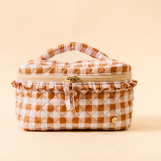 The Darling Effect’s Maple Gingham Glam & Go Quilted Cosmetic Bag features tan and white gingham fabric, a ruffled edge, zipper closure, and a handy top handle—ideal for use as a travel organizer. It’s photographed against a solid cream background.