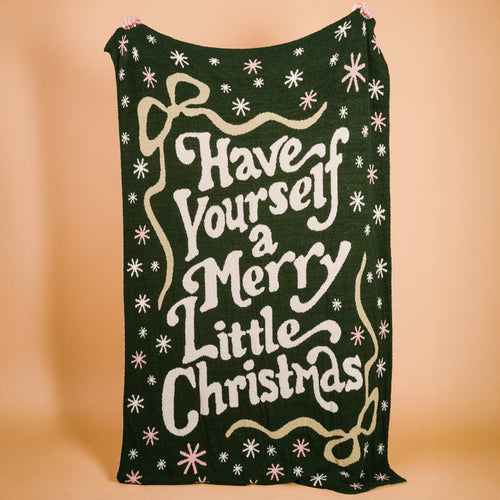 A dark green Merry Little Christmas Cozy Dreams Luxe Blanket by The Darling Effect, made of polyester microfiber, features white and light green holiday text with stars and bows, shown against a plain beige background.