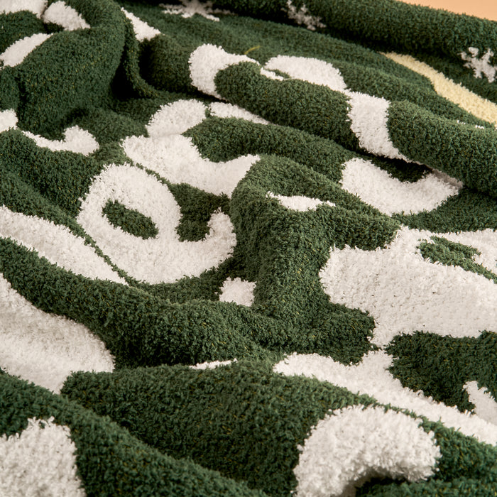 A close-up of The Darling Effect's Merry Little Christmas Cozy Dreams Luxe Blanket in green and white, showcasing its ultra-soft microfiber, bold abstract pattern, and cozy folds that highlight its inviting warmth.