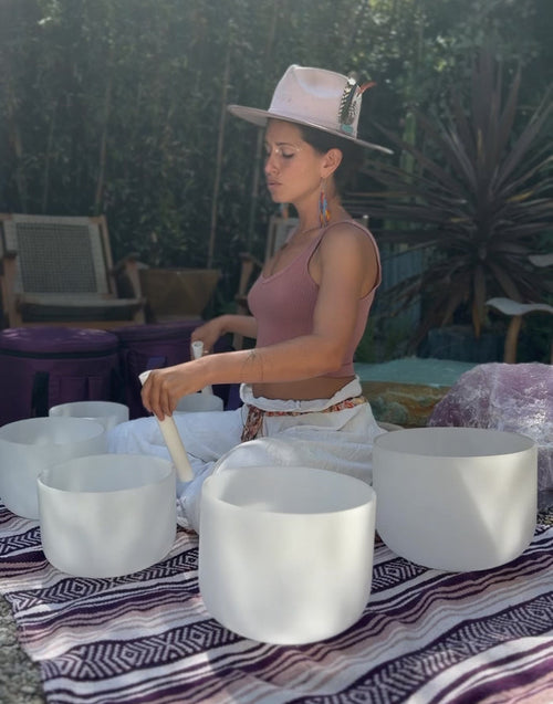Woman playing white singing bowls outdoors with plants and furniture in the background