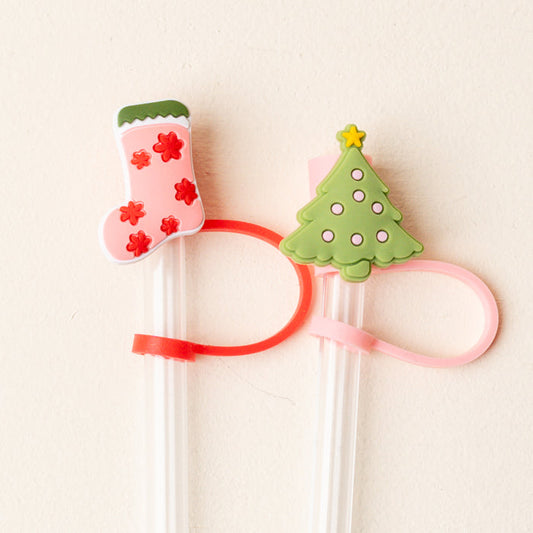 The Darling Effect's Naughty or Nice Straw Topper Set includes two white chopsticks with pink and red bands, festive silicone toppers—a Christmas stocking and a green tree with a star—adding leak-resistant holiday flair to your drinkware.