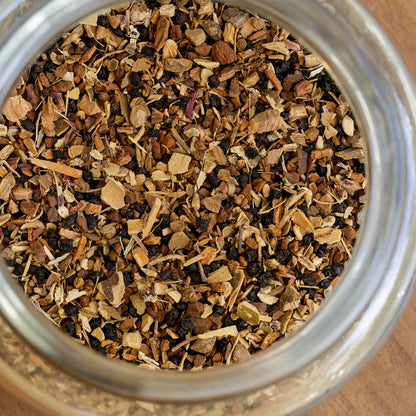 Close-up of a glass jar filled with dried herbs and spices on a wooden surface.