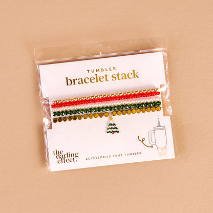 The Darling Effect's O Christmas Tree Tumbler Bracelet Stack features four festive beaded bracelets with red, white, green, and gold beads plus a Christmas tree charm—perfect accessories for your 40 oz tumbler and displayed on a beige background.