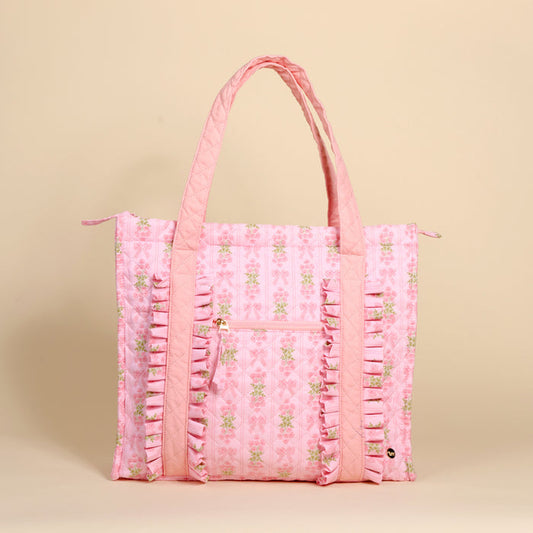 The Darling Effect's Oh So Fancy Pink The Everyday Quilted Tote Bag features floral quilted fabric, vertical ruffles, a front zipper pocket, sturdy handles, trolley sleeve, and zip closure—all shown against a light beige background.