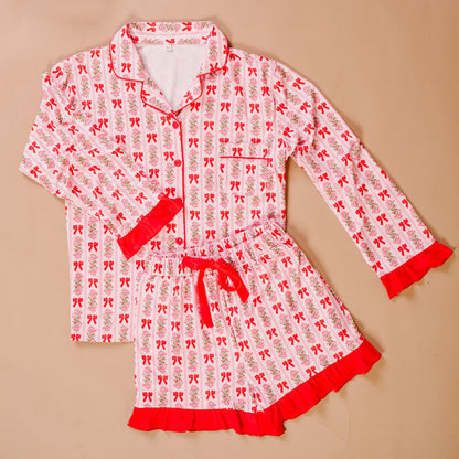 The Darling Effect’s Oh So Merry Sweet Dreams Pajama Shorts Set features pink and white stripes, floral and bow prints, ultra-soft fabric, red trim, and ruffled collar, cuffs, and shorts hem for a cozy lounge experience.