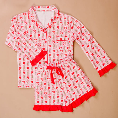 The Darling Effect’s Oh So Merry Sweet Dreams Pajama Shorts Set features pink and white stripes, floral and bow prints, ultra-soft fabric, red trim, and ruffled collar, cuffs, and shorts hem for a cozy lounge experience.