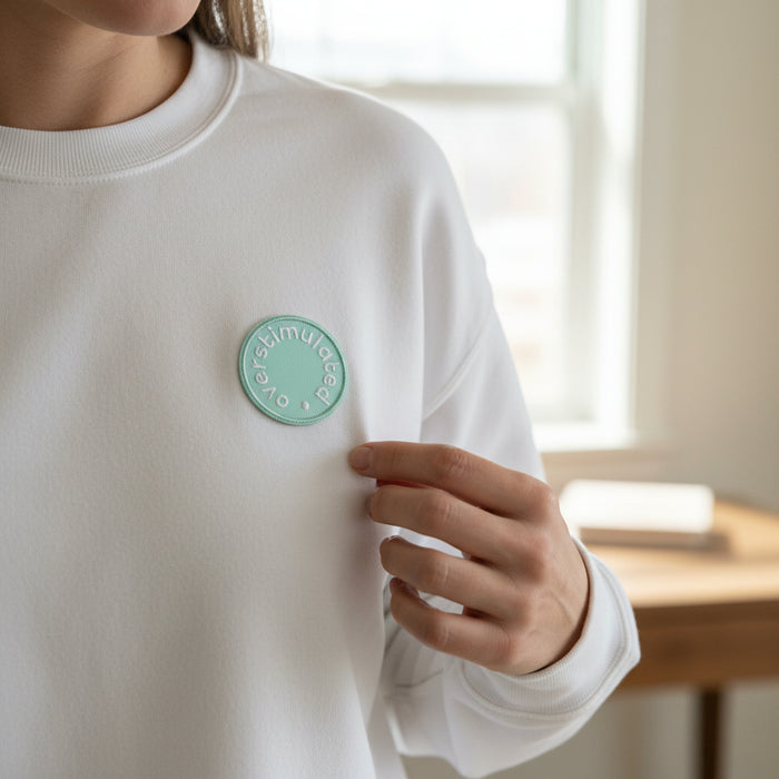 The Darling Effect's Overstimulated Mix & Match Iron-On Patch—a round mint green embroidered patch—lets you easily customize your look with colorful style. Shown on a white sweatshirt, held near a sunlit window.