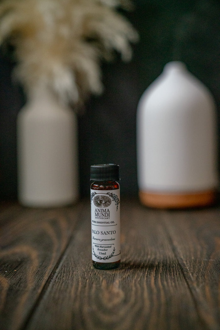 Small bottle of Anima Mundi Palo Santo oil on a wooden surface with decorative vases in the background.