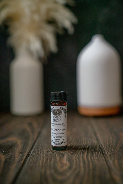 Small bottle of Anima Mundi Palo Santo oil on a wooden surface with decorative vases in the background.